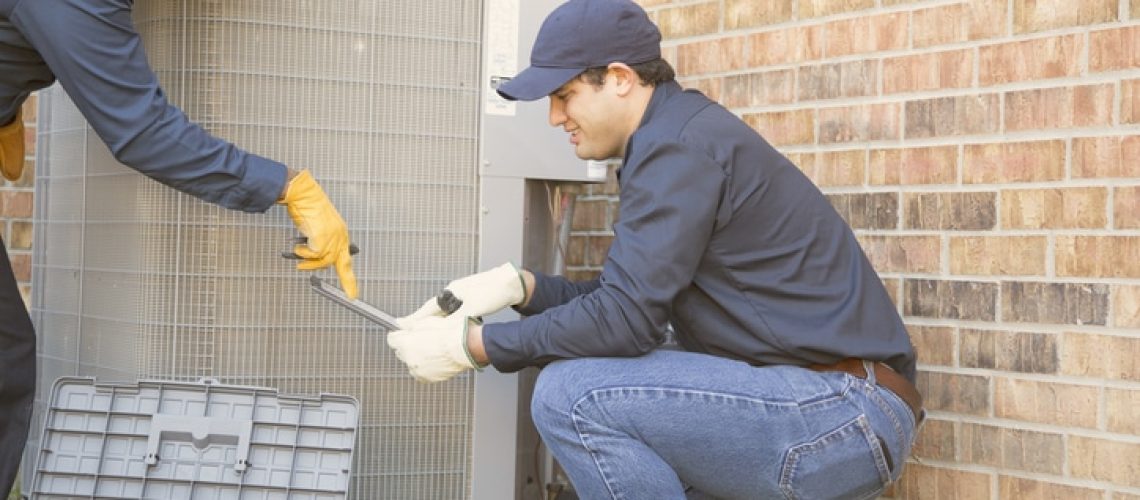 Multi-ethnic team of blue collar air conditioner repairmen at work.  They refer to digital tablet and carry tools and tool box.